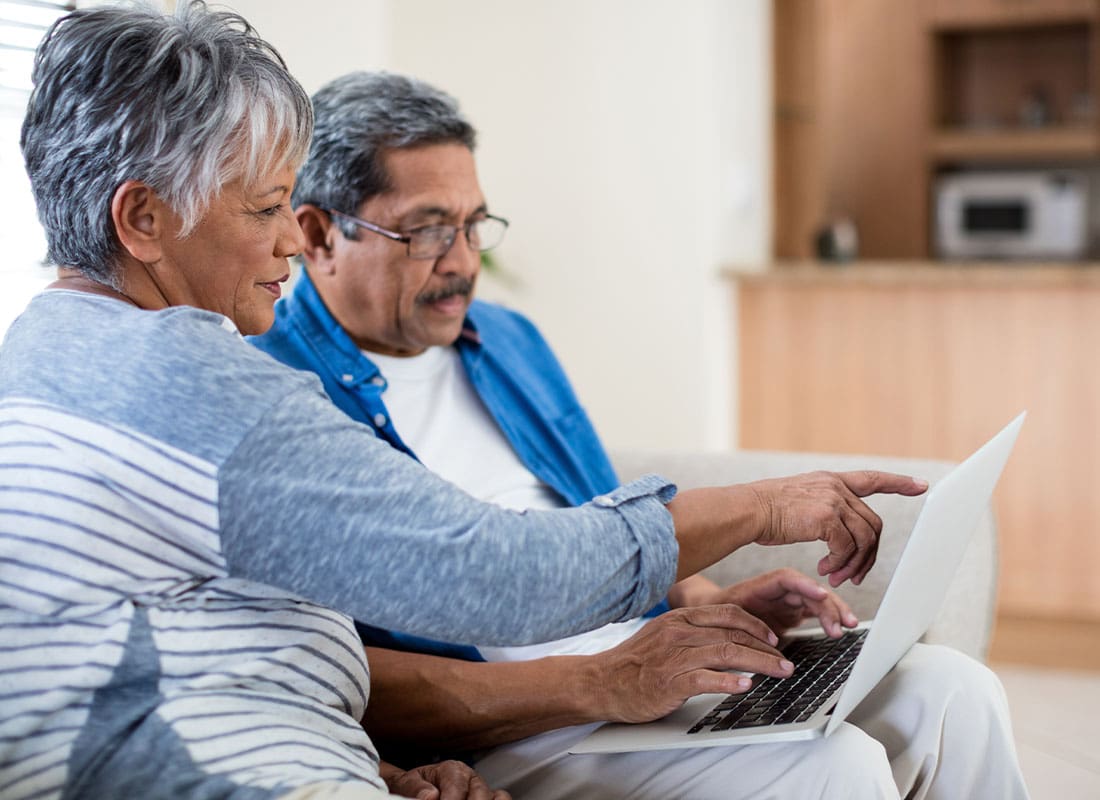 ACA and Short-Term Medical Plans - Senior Couple Sitting in a Well Lit Living Room on the Sofa and Reviewing Medicare Coverage on a Laptop